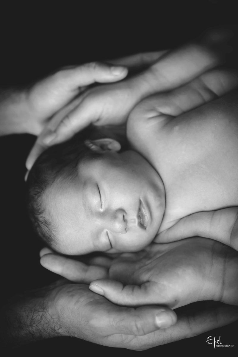 photo studio bébé fond noir dans les mains de ses parents