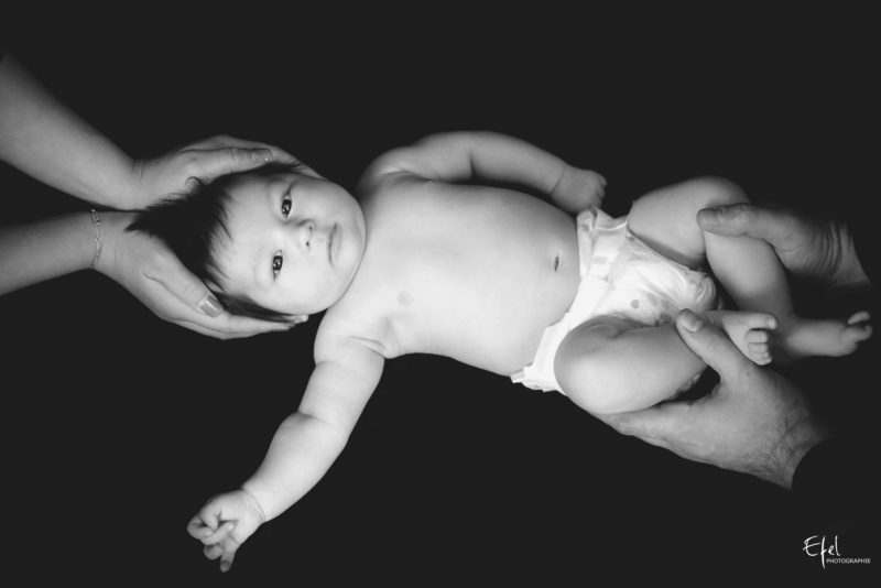 Bébé fille de deux mois entre les mains de ses parents - photographe hautes alpes